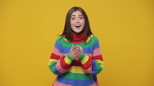 Excited pretty young woman 20s years old in colorful sweater isolated on yellow background studio. People lifestyle concept. Put palms folded on chest showing shape heart with hands heart-shape sign