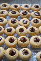 Light brown beige baked peanut cookies filled with dark chocolate, one by one on metal grid, tasty Christmas sweets ready to eat