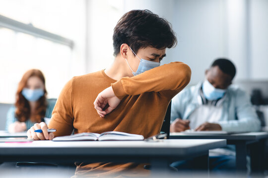 Asian male student couching in his elbow, sneezing in sleeve