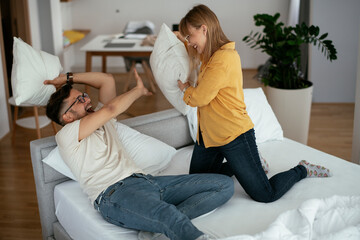 Husband and wife fighting pillows on the bed. Young couple having fun at home.