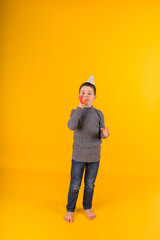 boy toddler with a festive whistle and a hat on a yellow background in full growth