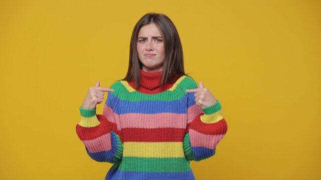 Shocked confused young woman 20s years old in colorful sweater posing isolated on yellow background studio. People lifestyle concept. Looking camera pointing fingers herself ask say who me no thanks