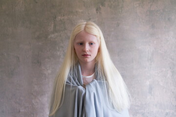 Medium horizontal natural light portrait of beautiful legally blind blue-eyed albino young girl draped in shawl looking straight ahead - obrazy, fototapety, plakaty