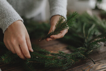Close up of female hands holding fir branches and making rustic christmas wreath on wooden table