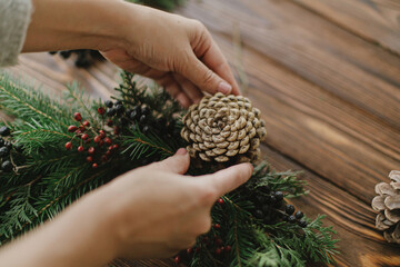 Making rustic christmas wreath, seasonal winter workshop. Florist hands holding pine cone