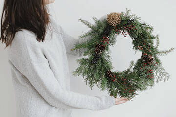Woman in sweater holding modern rustic christmas wreath on white background. Merry Christmas © sonyachny