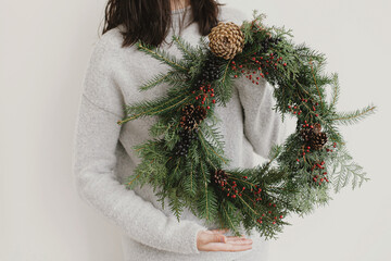 Rustic christmas wreath in female hands on background of white wall. Merry Christmas © sonyachny