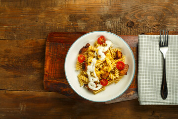 Pasta with chicken and cheese in a gray plate on a stand on a napkin with a fork.