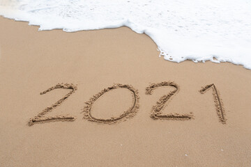 Happy New Year 2021 sign on the sea beach with soft wave of white foam. Welcoming 2021 with new resolutions, dreams concept.
