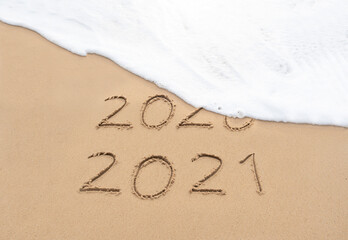 Goodbye 2020 Happy New Year 2021 sign on sandy beach with foam wave. Handwritten 2020 and 2021 on beautiful sand beach. New Years 2021 replace 2020 concept