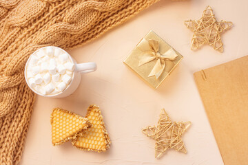 Fototapeta na wymiar Cozy home still life: white cup with cocoa with marshmallows, cookie, chunky knit scarf, golden gift box and decorative stars. The concept of coming winter, christmas eve and new year. Warm shades..