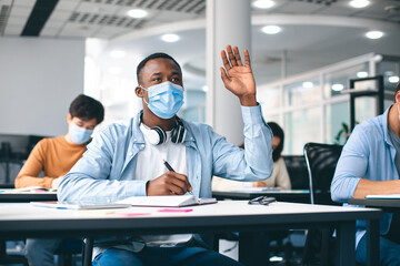 Black male student raising hand, wearing medical mask
