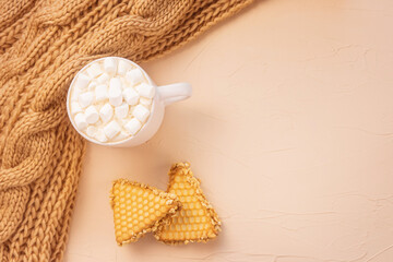 Cozy home still life: a white cup with cocoa with marshmallows, cookie, chunky knit scarf. The concept of the coming winter, christmas eve and new year. Warm shades, close-up...