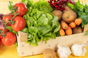 Fresh vegetables in a wooden box on a yellow table
