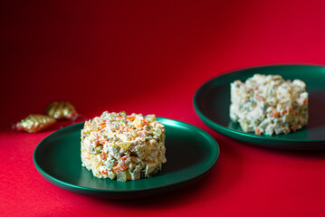 Traditional Russian salad called Olivier served on a green plate on a red background. Festive salad of meat and vegetables. Concept for a Christmas or New Year dinner. Front view. Copy space 