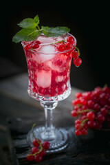 Summer drink with white sparkling wine. Homemade refreshing fruit cocktail or punch with champagne, red currant, ice cubes and mint leaves on a dark wooden background