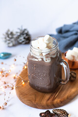 Cocoa drink with marshmallows in a glass mug, served on a light marble table with Christmas festive decorations. Winter mood. Close-up. Selective focus