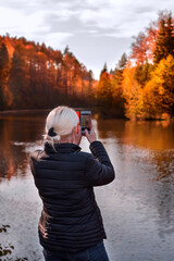 a woman takes photos of the autumn landscape on her smartphone