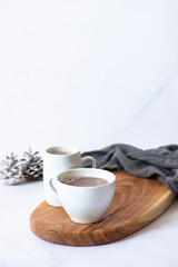 Two white cups with hot chocolate or cocoa drink on a wooden board on a light marble background with festive winter decorations. Winter mood. Frontal view. Copy space. Selective focus