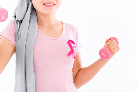 Asian women attach a pink ribbon to their tops. Doing exercise by lifting pink dumbbells on color background. breast cancer concept, cancer prevention concept.