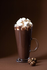 Cocoa drink with marshmallows in a glass on a brown background with festive winter decorations. Winter mood. Minimalistic monochrome composition. Selective focus. Frontal view. Vertical. Copy space