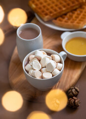 Fototapeta na wymiar Winter sweet breakfast with cocoa drink with marshmallows, waffles, honey, served on a wooden board and a brown background with festive Christmas decorations. Winter mood. Close-up. Selective focus 