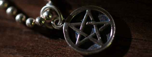 Silver Pentagram charm old necklace on a dark brown wooden surface, light and shadows contrasts,...