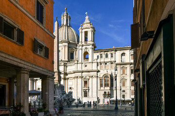 Fototapeta na wymiar View of the Sant'Agnese in Agone church, the Fountain of the Four Rivers with obelisk and tourists in silhouette from an alleyway leading to the Piazza Navona in Rome Italy.