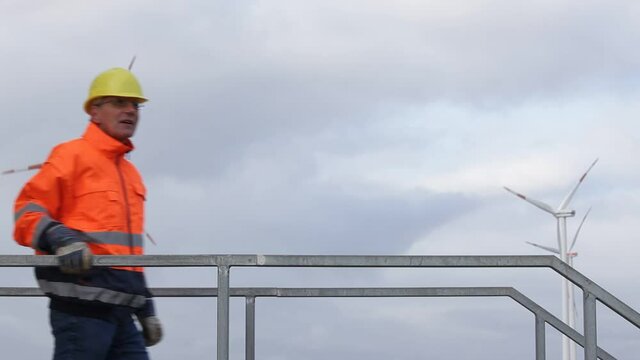 Mature engineer walking in front of wind turbines with protective workwear