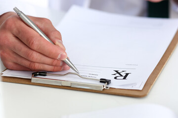 Male doctor hand write prescription at office worktable using silver pen. Panacea, life save, prescribing antidepressant, legal drug store, vitamin aid, ward round, give or take potion concept