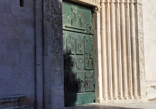 Porta in bronzo entrata principale antica chiesa gotica con bassorilievi e colonna in un giorno esstivo ombra e sole 