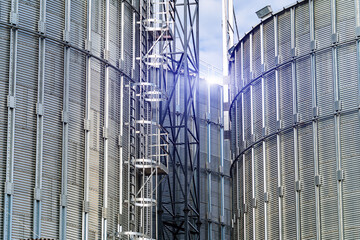 Metal grain elevators on modern factory. Crop storage in factory. Selective focus on steel constructions.