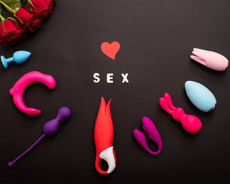 The inscription sex is a heart of roses and a collection of vibrators on a black background. Sex toys of various shapes. Assortment of sex shop