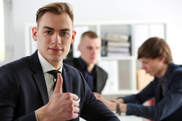 Male hand showing OK or approval sign with thumb up in creative people office during conference. High level and quality service, job offer, excellent education, advisor, serious business concept