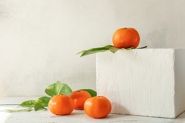 Fototapeta na wymiar Composition of tangerines with leaves on a box and a light wooden background. Symbol of Christmas and new year.