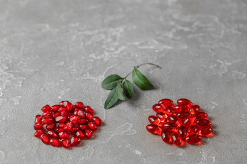 red pomegranate berries with leaves and vitamins in capsules on a rough gray background Concept of healthy nutrition, vitamins and nutritional supplements