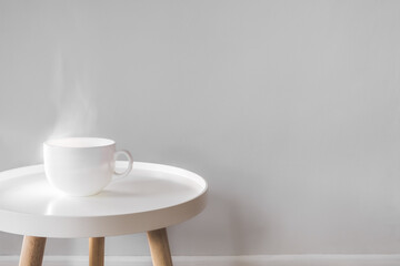 Mug with hot drink on a white coffee table indoors. Scandinavian interior style, minimalism in house, tranquil living concept