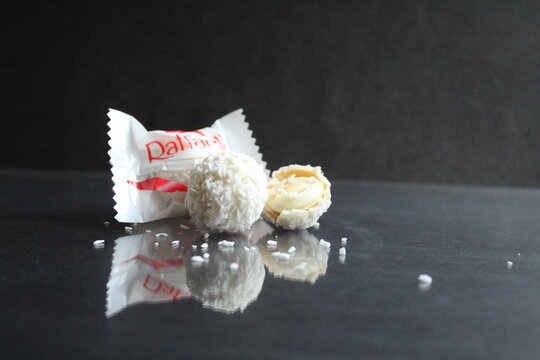 candy white and Raffaello lie together side by side on a black glossy mirror background with a reflection from the copy space free space for the text of the product