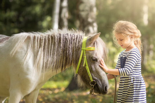 Little blond girl caressing the little horse pony and hugging it