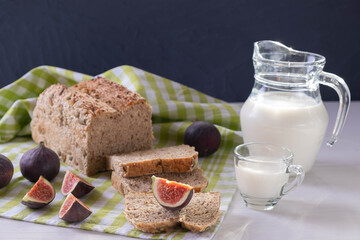 on the table a tablecloth, freshly sliced bread, a jug and a mug of milk, ripe figs