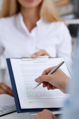 Female arm in white shirt offer contract form on clipboard pad and silver pen to sign closeup....