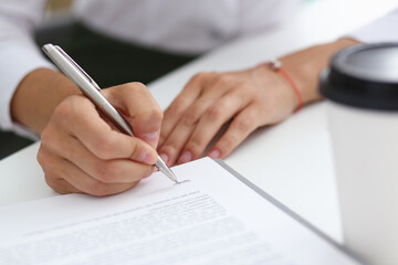 Female hand holding silver pen ready to make note in opened notebook sheet. Businesswoman coffee cup workspace make thoughts records at personal organizer, white letter collar conference, signature