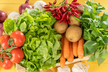 Fresh seasonal vegetables in a wooden basket on a yellow table