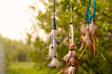 Dream catchers evolve in the wind, against a blurred green background of plants with copy space,...