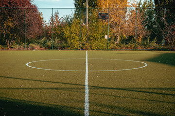 Turf soccer/football field behind the steel strings, autumn scene with orange yellow trees around. Selective focus.