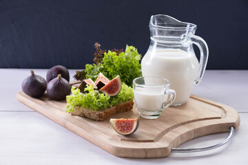 there is a board on the table with freshly sliced bread, a jug and a mug of milk and ripe figs on it