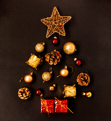 Creative idea Christmas or New Year tree made of gold and red balls, stars, gift boxes, drums and fir cones on a black background.