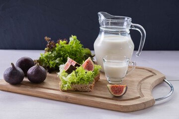 freshly sliced bread, a jug and a mug of milk, ripe figs and green lettuce are on the table