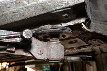 Close-up on the arm of a car lift based on a car chassis in the background of the workshop.