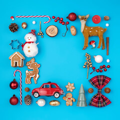 Christmas holiday decorative border frame made with candy cane, ornaments, snowman, deer and gingerbread man on blue background. Minimal winter or New Year concept with copy space. Flat lay, top view.
